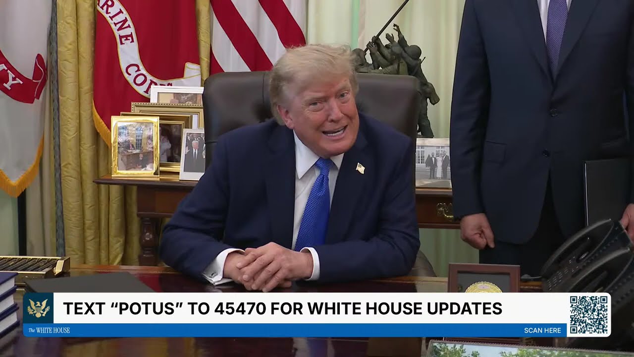 President Donald Trump smiles while seated at the Resolute Desk during a White House signing session.
