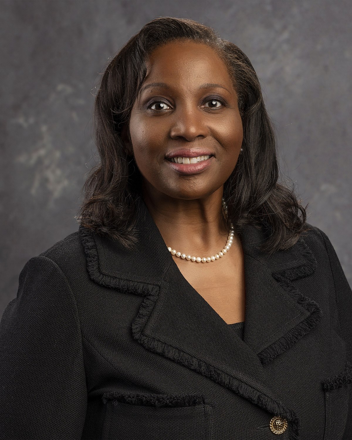 Federal Reserve Governor Lisa D. Cook in an official head-and-shoulders portrait against a gray background.